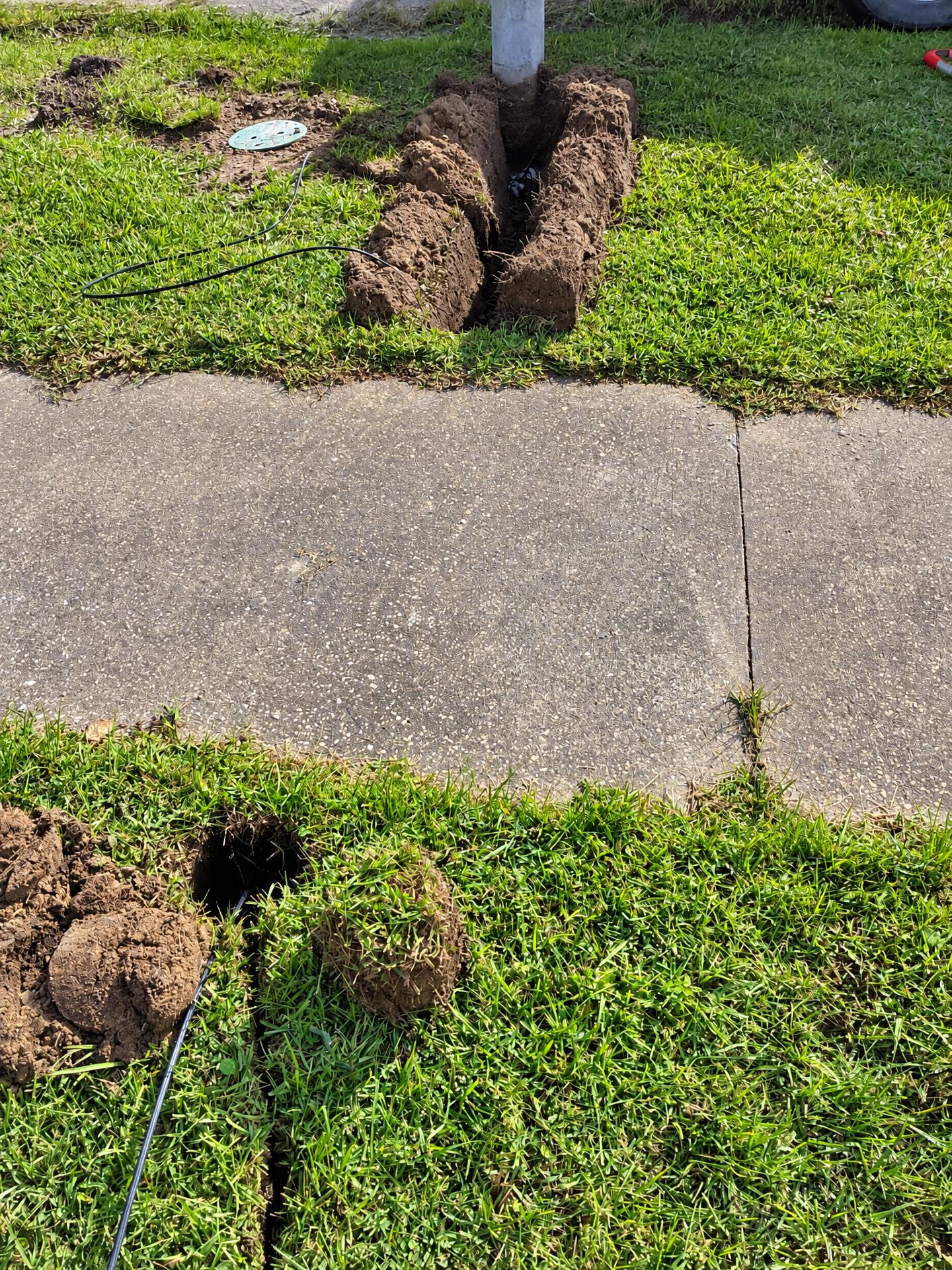 Narrow trench and bore pits for a fiber drop beside a sidewalk